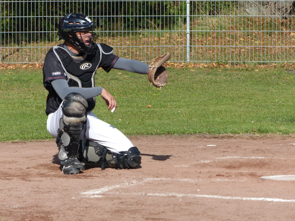 Catcher in schutzausrüstung fängt einen ball mit seinem handschuh auf einem baseballfeld