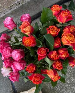 Ein strauß lebhafter rosa und orange rosen, die auf einer grauen betonoberfläche liegen, mit einem sichtbaren blätterwerk und im fokus stehenden blüten.